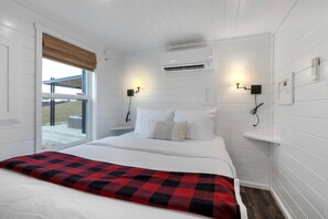 A hotel room with a bed, two bedside tables, an air conditioning unit, and a window with a view. - Scenic Hill Country Tiny Home with Pool & Community Amenities Near Fredericksburg, TX (Fredericksburg)