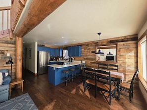 A spacious kitchen with a central island, blue cabinets, and a dining area with wooden chairs and a table. - Charming Home with Golf Course Views & Relaxing Vibes in McCall, Idaho (McCall)