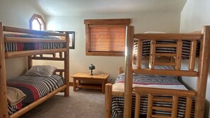 Une chambre avec des lits superposés, une petite table avec une lampe et une fenêtre avec des stores.