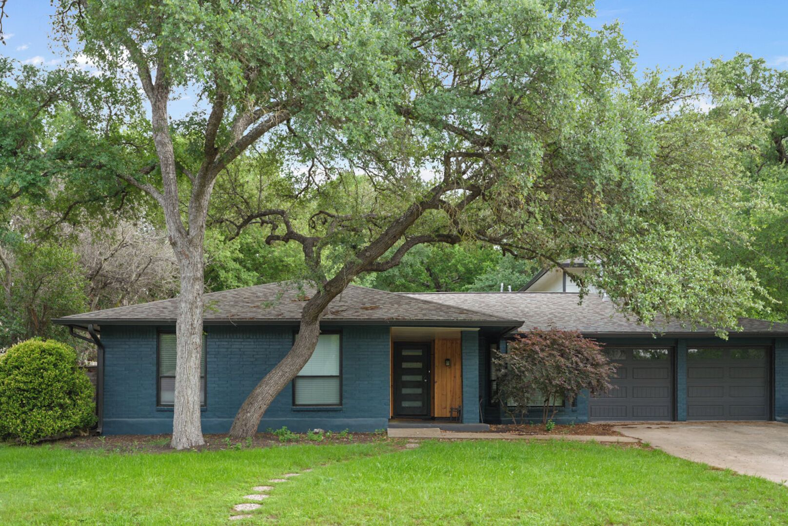 A single-story house with a front door, a garage, and a large tree in front.