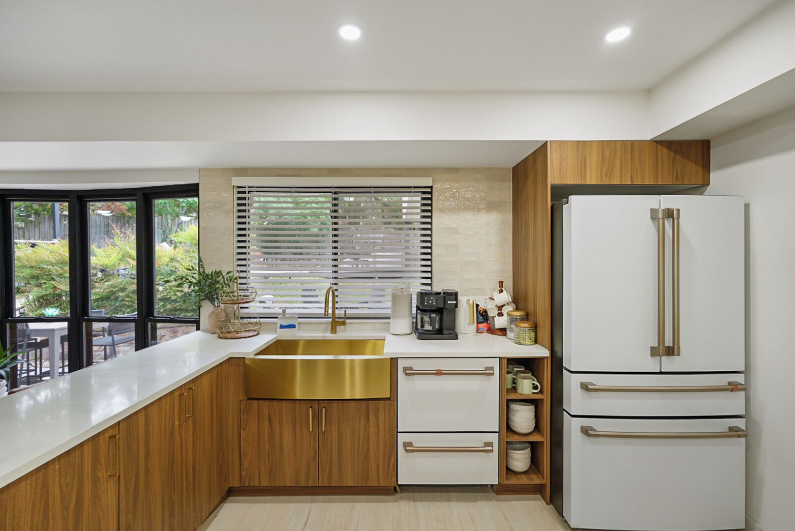 Una cocina moderna con un lavamanos grande, armarios de madera, un refrigerador blanco y una ventana con persianas.