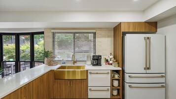 Una cocina moderna con un lavamanos grande, armarios de madera, un refrigerador blanco y una ventana con persianas.