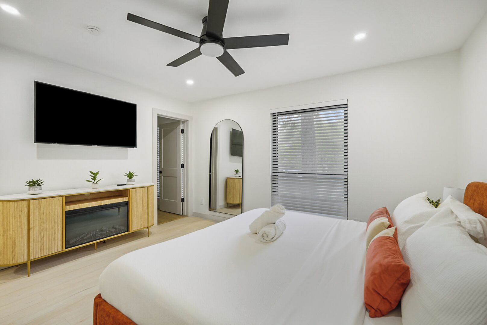 A modern bedroom with a bed, TV, ceiling fan, and a small cabinet.