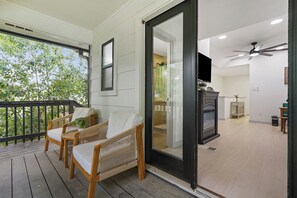 A wooden deck with two wicker chairs, a glass door leading to a room with a fireplace, and a ceiling fan. - Forest Bend (Austin)