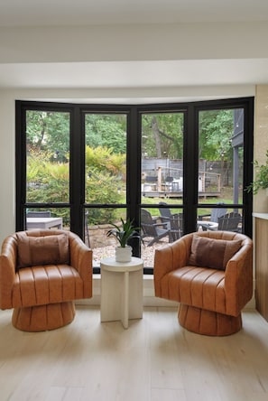 A room with two leather armchairs facing a large window with a view of a backyard. - Forest Bend (Austin)