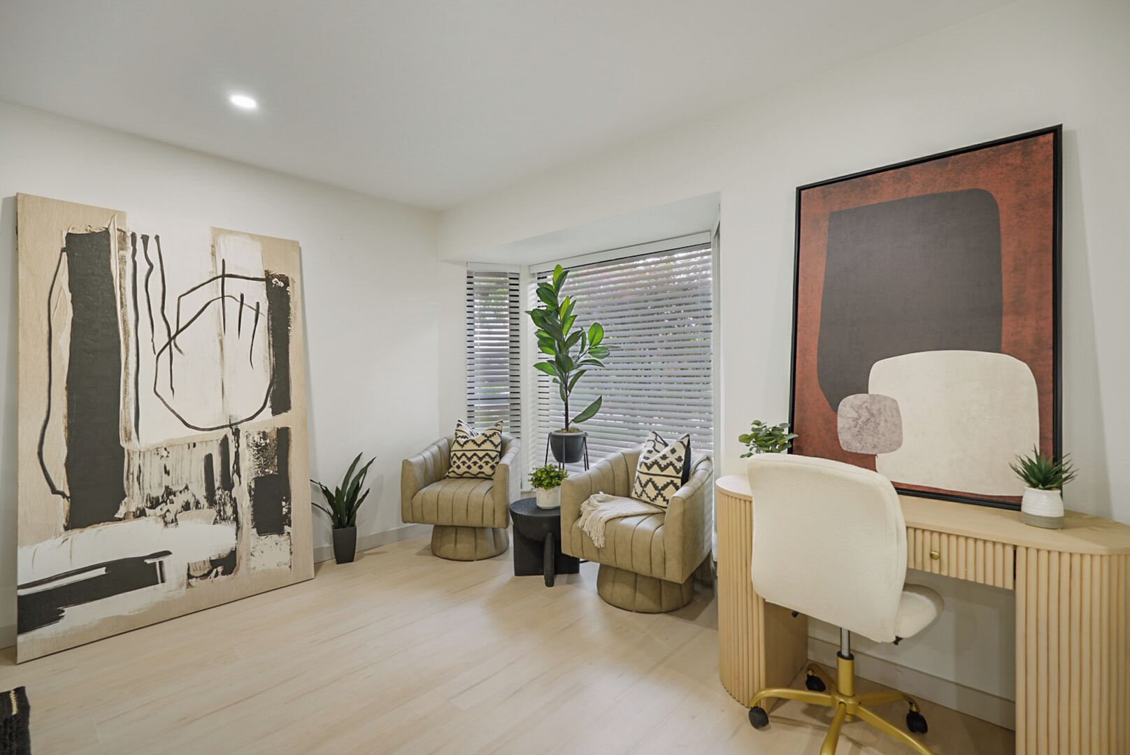 Un salon moderne avec un grand tableau abstrait, un bureau avec une chaise et deux canapés agrémentés de coussins décoratifs.