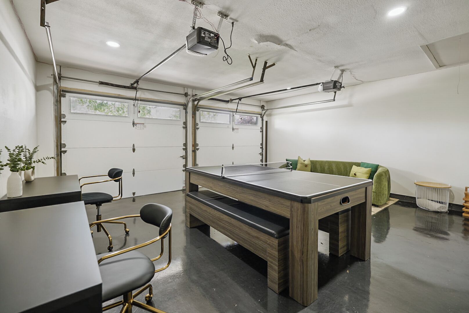 A room with a ping pong table, chairs, a sofa, and a projector mounted on the ceiling.