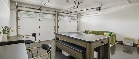 A room with a ping pong table, chairs, a sofa, and a projector mounted on the ceiling.