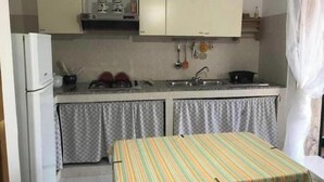 A compact kitchen with a refrigerator, stove, sink, and a striped table. - The Terrace of Campomarino (Campomarino di Maruggio (TA))