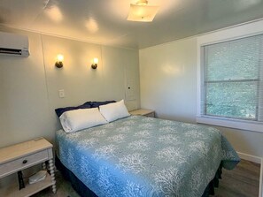 Ein Schlafzimmer mit einem Bett, Nachttischen, einer Klimaanlage, Wandleuchten und einem Fenster mit Jalousien.