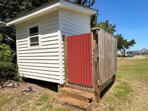 A small, single-story structure with a red door and a wooden staircase leading to a porch. - Ocracoke Local 5: Close to Harbor | Private Boat Slip | Queen Bed (Ocracoke)