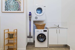 A laundry area with a washing machine, a dryer, a mop, and a wicker basket on the dryer. - 14A Archerfield Dr (Shell Cove)