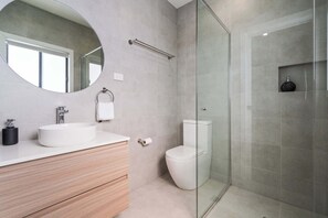 Un bagno moderno con uno specchio rotondo, un lavandino bianco, un water e un box doccia in vetro.