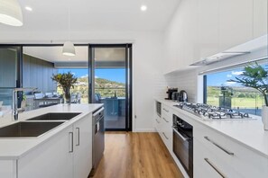 A modern kitchen with a large island, a gas stove, and a view of the outdoors. - 14A Archerfield Dr (Shell Cove)