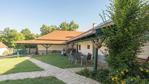 A covered outdoor seating area with a patio table and chairs, a brick pathway, and a garden with yellow flowers.