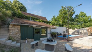 A stone building with a green door, outdoor seating, a barbecue, and a pool.