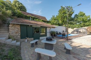 Un bâtiment en pierre avec une porte verte, des places assises à l’extérieur, un barbecue et une piscine.