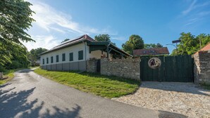 A two-story house with a paved driveway, a stone wall, and a green gate.