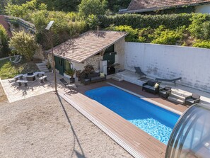 Una piscina con solárium, asientos exteriores y un pequeño edificio con techo inclinado.