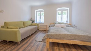 A room with a bed, a sofa, a small table, and two windows.