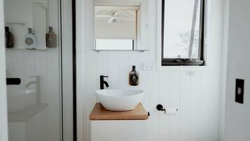 Une salle de bain moderne avec un lavabo sur colonne blanc, un robinet noir et une étagère en bois.
