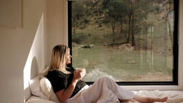Une personne assise sur un lit, près d’une fenêtre, tenant une tasse.