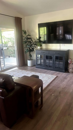 Ein Wohnzimmer mit Sofa, Couchtisch, Wandfernseher, Schrank und einer Topfpflanze.