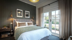 A bedroom with a bed, two wall-mounted lamps, a nightstand with a plant, and a window with curtains.