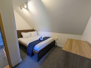 Ein Schlafzimmer mit einem Bett, einem Nachttisch, einer hölzernen Bank und einer Deckenleuchte.