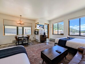 A hotel room with two beds, a TV, a dining area, and large windows with mountain views. - New Listing | Updated | Walk to Slopes (Keystone)