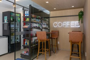Een modern koffiebar interieur met een glazen koelkast vol drankjes, houten barstoelen en een neonbord waarop 'COFFEE' staat.