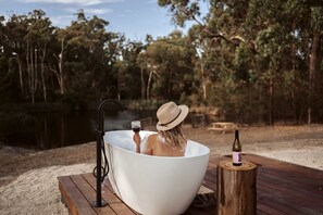 A person relaxing in a large white bathtub outdoors, surrounded by trees and a wooden deck. - Secluded Tiny Home with Bird-Watching Hut near Loch, Victoria (Loch)