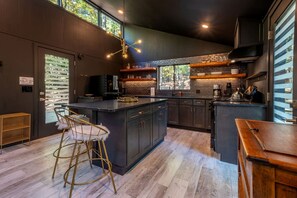 A modern kitchen with dark cabinetry, a central island, and a bar area. - Modern Forest Cabin with Hot Tub, Screened Porch & Resort Access Near Hedgesville, WV (Hedgesville)