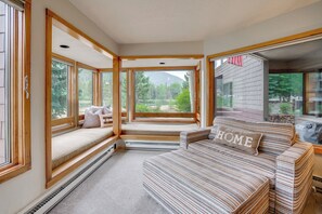 A room with a large window, a sofa with a 'HOME' pillow, and a view of a forested area. - Keystone Lakefront Retreat! Pool & Hot Tub Access (Keystone)