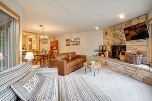 A living room with a stone fireplace, a leather sofa, and a dining area with wooden furniture. - Keystone Lakefront Retreat! Pool & Hot Tub Access (Keystone)