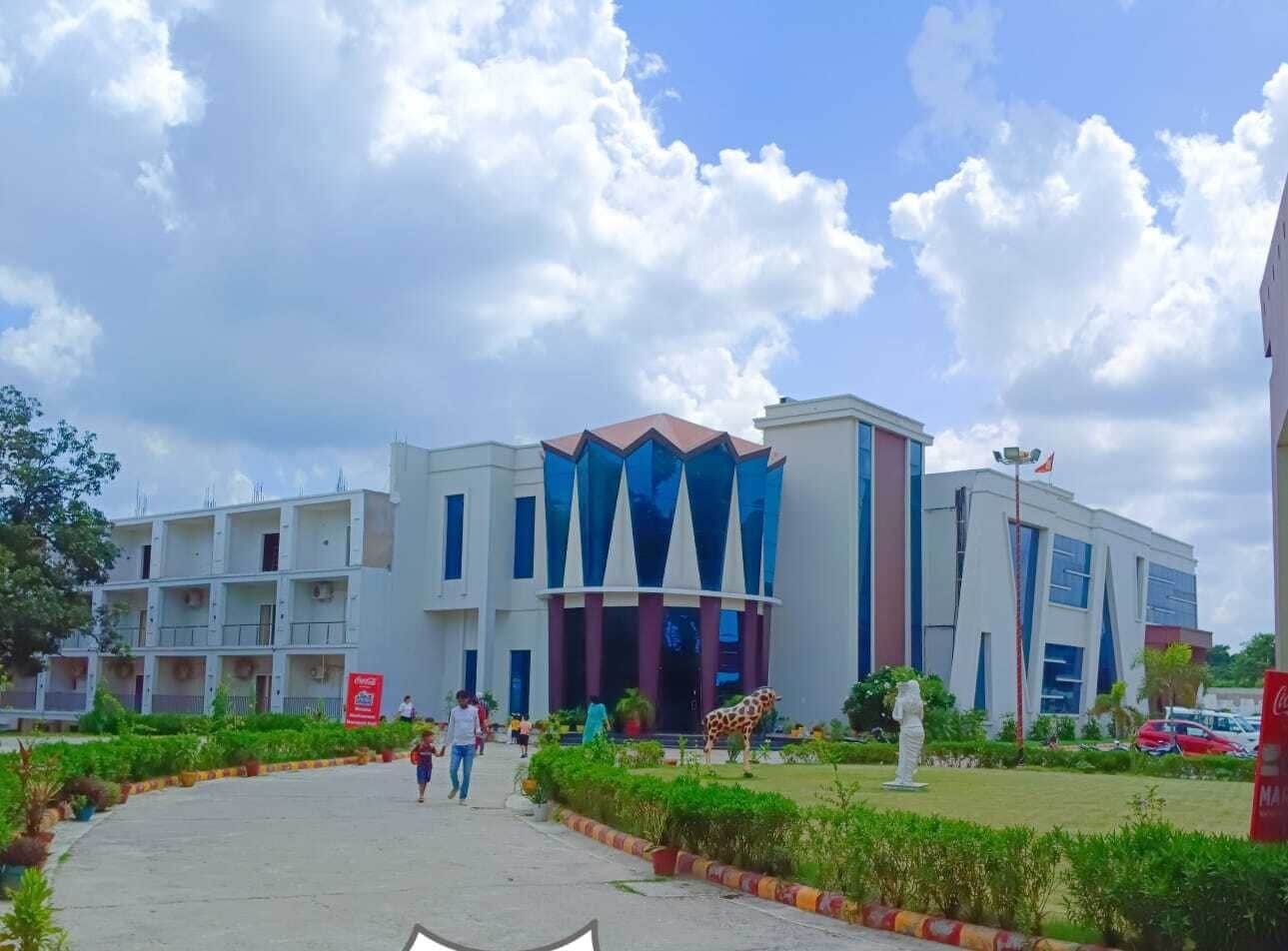 A multi-story building with a central entrance, surrounded by greenery and a parking area.