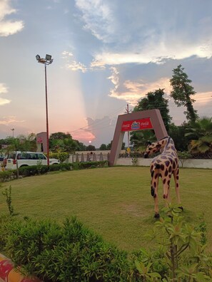 Una estatua de jirafa en un área con césped, con un cartel de Coca-Cola al fondo.