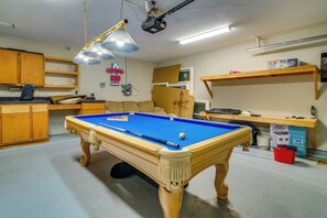 Una mesa de billar en una habitación con armarios de madera, un proyector instalado en el techo y un letrero de neón.