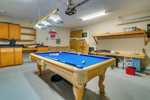 Uma mesa de bilhar em um espaço com armários de madeira, projetor no teto e um letreiro de neon.