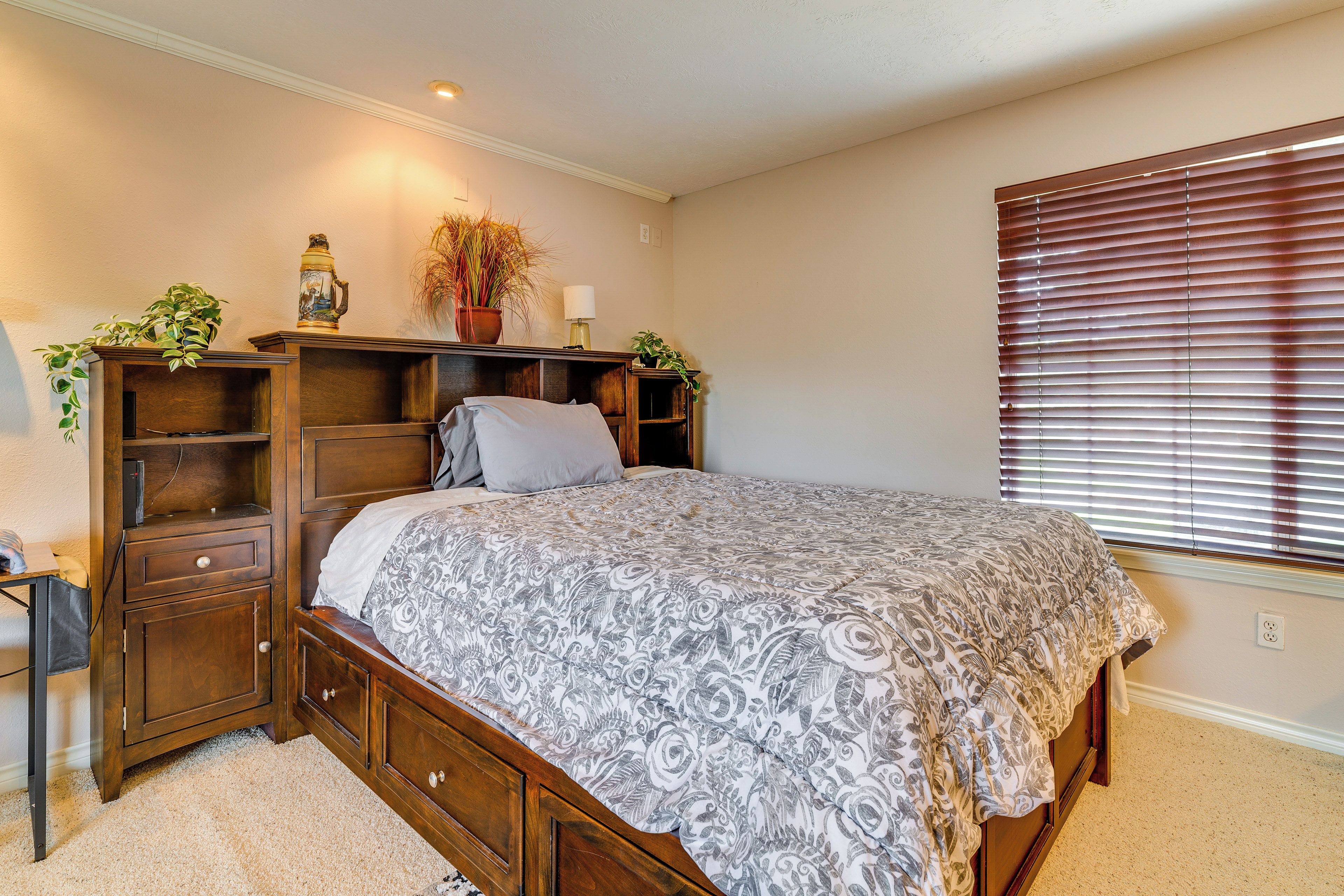 A bedroom with a bed, wooden nightstands, a dresser, and a window with blinds.