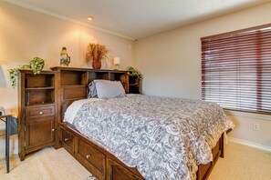 Un dormitorio con una cama, mesitas de noche de madera, un aparador y una ventana con persianas.
