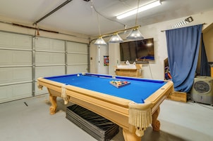 A pool table in a garage with a garage door, a ceiling fan, and a blue curtain.