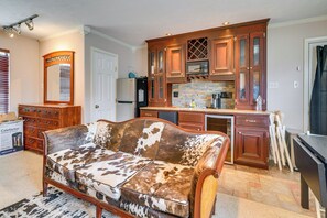 Ein gemütliches Wohnzimmer mit einem großen, gemusterten Sofa, Holzschränken und einer Steinrückwand in der Küchenzeile.