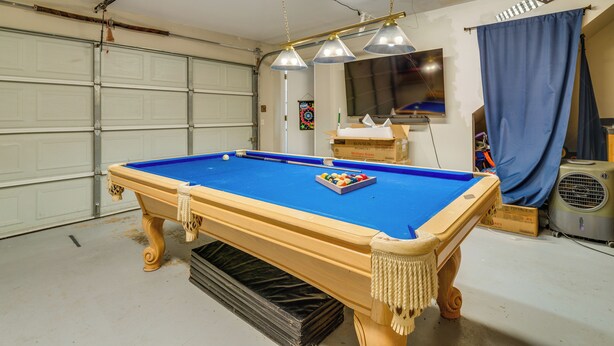 Ein Billardtisch in einer Garage mit Garagentür, Deckenventilator und blauem Vorhang.