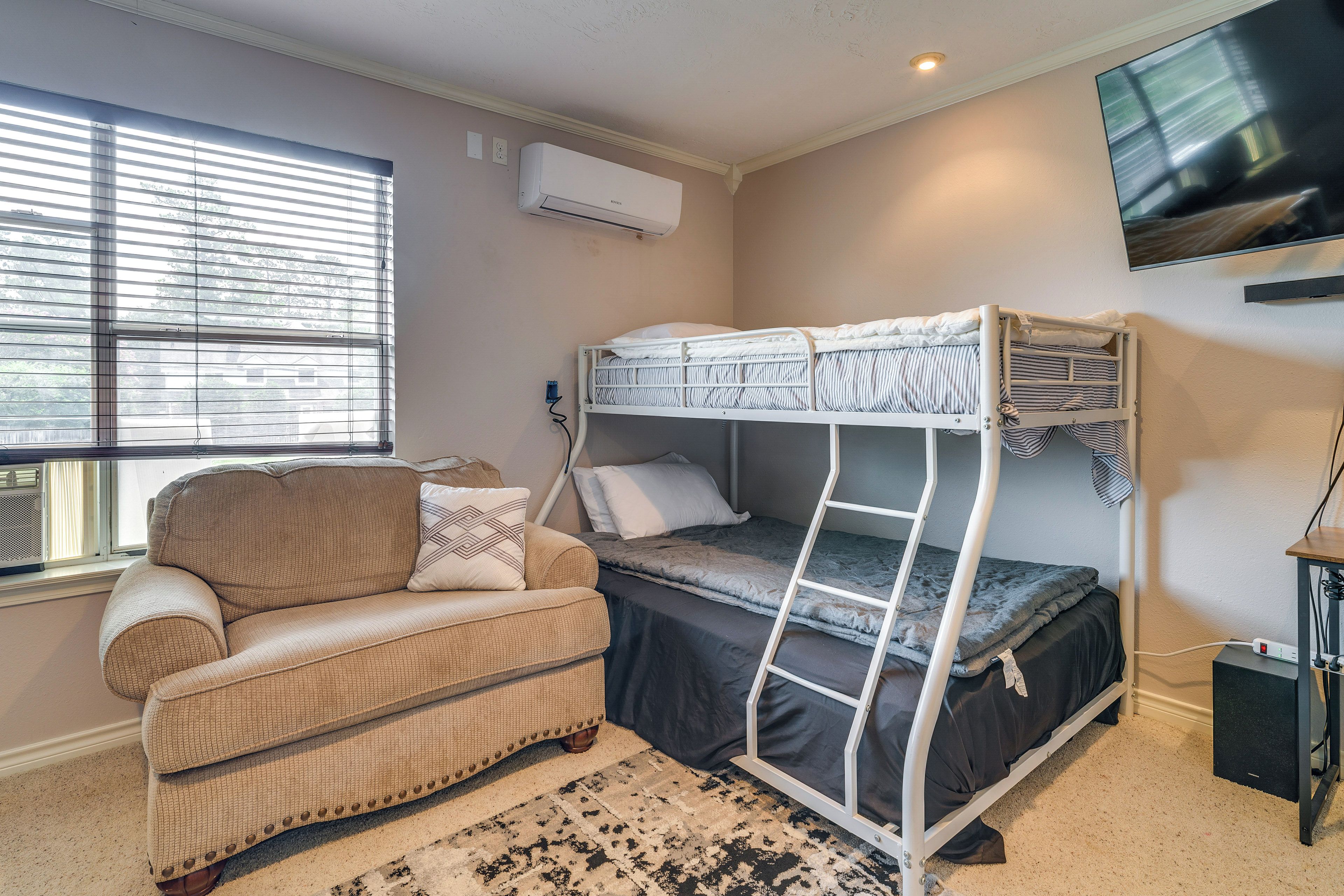 Ein Stockbett mit Fernseher darüber, eine Schlafcouch und ein Fenster mit Jalousien.