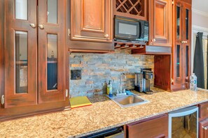 Una cocina con armarios de madera, protector contra salpicaduras de piedra, microondas, fregadero y escurreplatos.