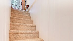 A carpeted staircase with a handrail, leading to a landing with a window and a door. - Deck & Mtn Views! Woodsy Haven in Running Springs (Running Springs)