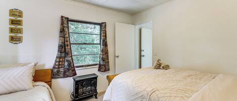A bedroom with two beds, a window with curtains, a heater, and a door.