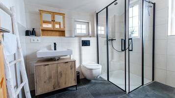Ein modernes Badezimmer mit Duschkabine aus Glas, einem hölzernen Waschtisch, einer weißen Toilette und einem Fenster über dem Waschbecken.