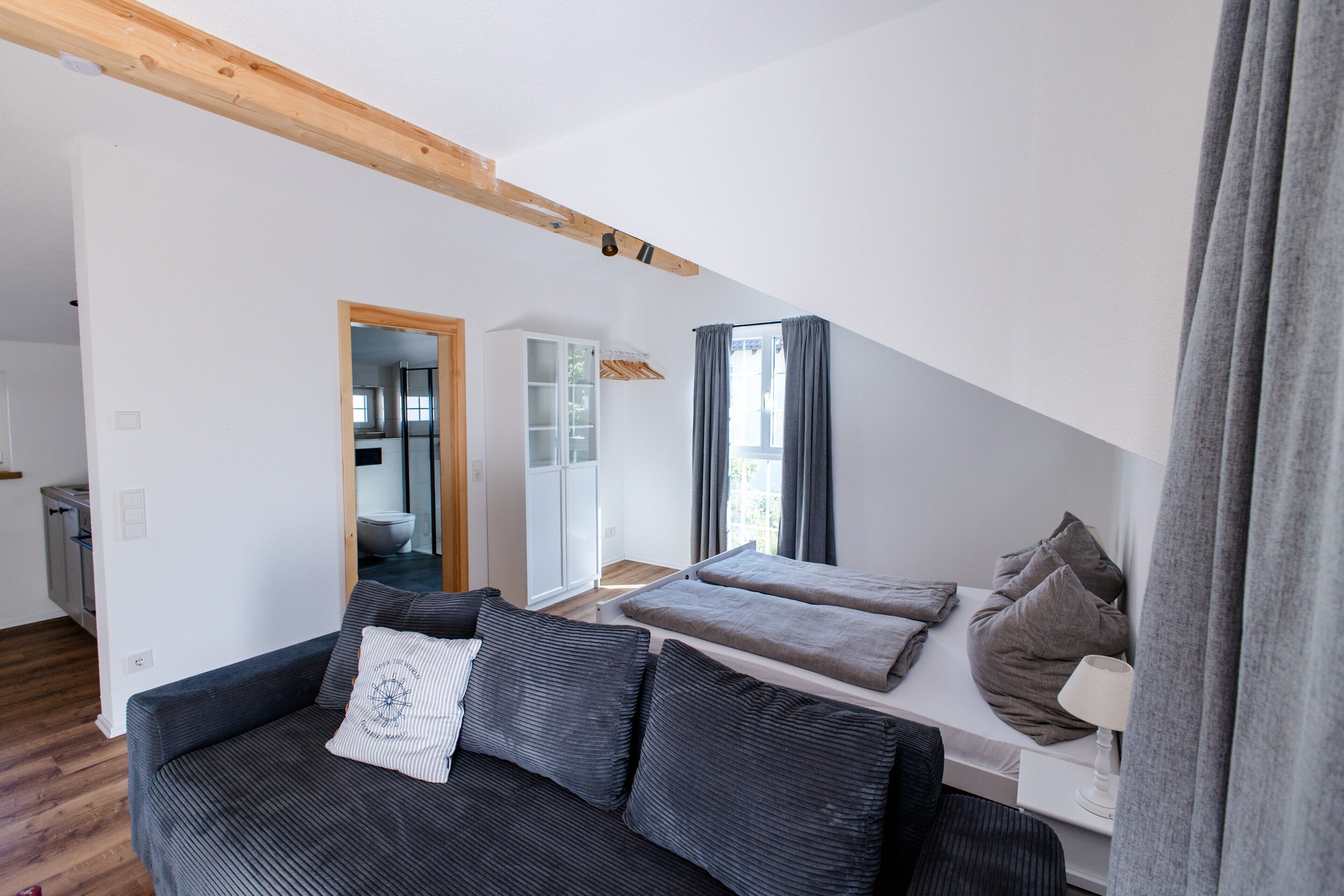 Ein modernes Wohnzimmer mit einem dunkelgrauen Sofa, einer weißen Kommode und Blick in ein Badezimmer durch eine offene Tür.